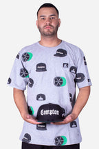 Camiseta Collab Starter x Compton Cap Cinza Mescla com estampa de bonés Compton, modelo segurando boné Compton.